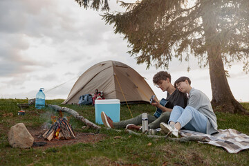 Man playing guitar for woman at fire and tent at nature. Romantic evening.