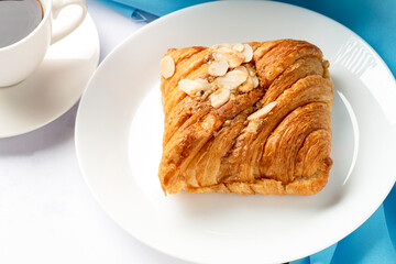 Almond croissant for breakfast on white plate with blue background, flat lay, top view.
