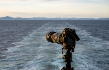 Professional dslr on tripod on back of cruise ship sailing away from Alaska coast leaving wake