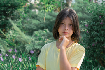 Portrait of a young girl in a yellow T-shirt, who lightly touches her chin with her hand.