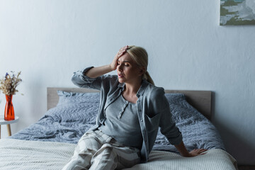 upset blonde woman with menopause suffering from migraine in bedroom. - obrazy, fototapety, plakaty