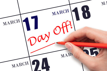 Hand writing text DAY OFF and drawing a line on calendar date 17 March. Vacation planning concept.