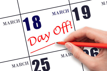 Hand writing text DAY OFF and drawing a line on calendar date 18 March. Vacation planning concept.