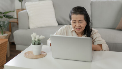 Happy and cheerful older lady Mature asian woman reading good news at laptop. senior business woman and technology concept.