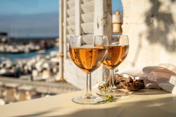 Summer party with cold rose wine in glass served on outdoor terrace in sunlights with view on old fisherman's harbour with colourful boats in Cassis, Provence, France