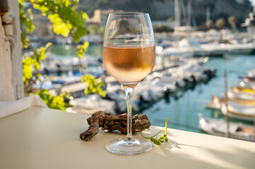Cold rose wine in glass served on outdoor terrace in sunlights with view on old fisherman's harbour with colourful boats in Cassis, Provence, France