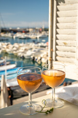 Cold rose wine in glasses served on outdoor terrace in sunlights with view on old fisherman's harbour with colourful boats in Cassis, Provence, France