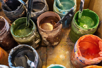 Open jars with multicolored paints in a cardboard box. Open paints in an art workshop. Creative activities