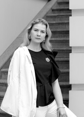 Black and white portrait of an elegant business woman in a stylish black blouse and a one-shoulder white jacket, looking into the camera. City building background. Women 40+ concept