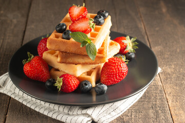 Fresh homemade food of berry Belgian waffles with honey, chocolate, strawberry, blueberry, maple syrup and cream. Healthy dessert breakfast concept with coffee