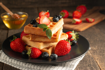 Fresh homemade food of berry Belgian waffles with honey, chocolate, strawberry, blueberry, maple syrup and cream. Healthy dessert breakfast concept with coffee
