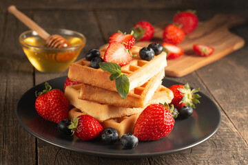 Fresh homemade food of berry Belgian waffles with honey, chocolate, strawberry, blueberry, maple syrup and cream. Healthy dessert breakfast concept with coffee