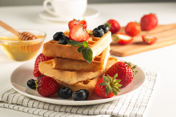 Fresh homemade food of berry Belgian waffles with honey, chocolate, strawberry, blueberry, maple syrup and cream. Healthy dessert breakfast concept with coffee