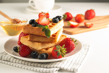 Fresh homemade food of berry Belgian waffles with honey, chocolate, strawberry, blueberry, maple syrup and cream. Healthy dessert breakfast concept with coffee