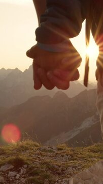 SLOW MOTION, LENS FLARE, CLOSE UP: Unrecognizable couple holding hands while hiking up to the mountaintop on a picturesque summer evening. Tourists in love enjoying a romantic hike and holding hands.