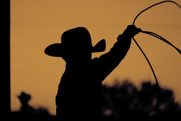 Western rodeo lifestyle shows child cowboy roping practice in silhouette at sunset.