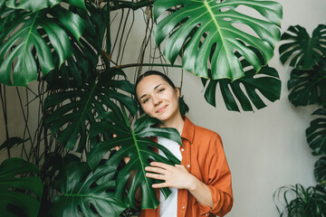A beautiful young smiling gardener woman stands in her flower shop among green plants. The concept of a green office, plant care, gardening, a modern green recreation area. © franz12