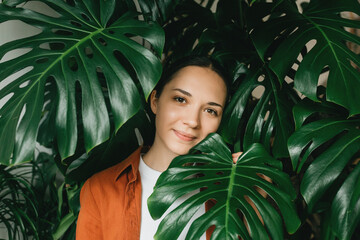 Close-up of the face of a beautiful young woman with natural make-up among large green tropical monstera leaves. © franz12