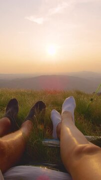 SLOW MOTION, CLOSE UP, SUN FLARE: Unrecognizable young couple moving their feet as they watch the sunset from their tent. Man and woman on summer hiking trip relax and watch idyllic evening nature.