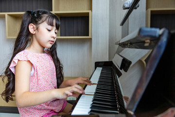 Cute Asian girl is practicing her classical piano lesson at home for song writing and music...