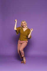 Naklejka premium full length of happy blonde woman in blouse having menopause and rejoicing on purple.