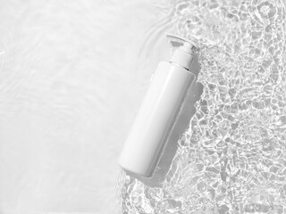 White cosmetic bottle on the water surface. Blank label for branding mock-up. Summer water pool fresh concept. Flat lay, top view.	