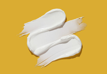 White cosmetic cream lotion swatch smear smudge on yellow background.