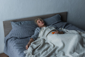 depressed blonde woman with menopause sleeping near pills in bed.