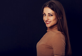 Fototapeta premium Beautiful young business toothy smiling woman thinking and looking happy on dark black background with empty copy space. Portrait