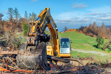 Mountainous terrain with an excavator bucket in the foreground. An excavator clears fallen trees after the natural disaster.