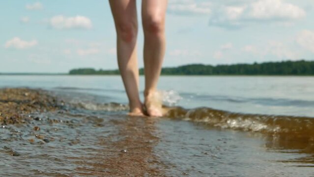 Woman walks on pebble river bank. Closeup view on female feet on pebble river or lake bank.