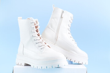 Two pairs of white demi-season boots made of eco-leather with fasteners and laces stand on a white...
