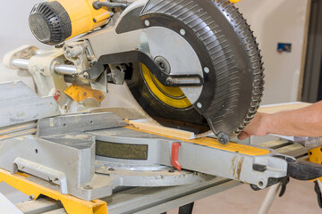 Using circular saw, a construction worker cuts wood moldings for baseboards during the finishing work process