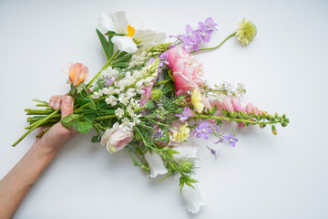Top view, chic wedding bouquet of delicate flowers, roses, peonies and wild and cultivated pink flowers on a light background in the hand of a florist