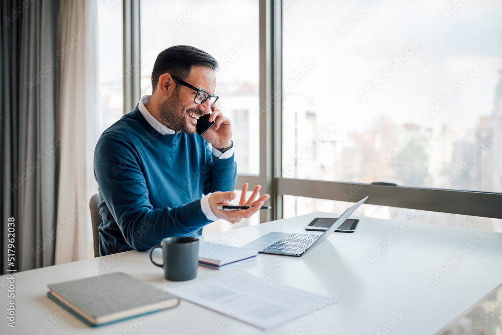 Wall mural smiling entrepreneur discussing on cellphone while using laptop.