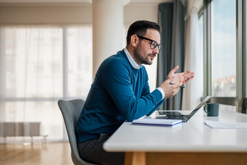 Confident businessman analyzing plan on laptop. Young professional working while sitting at desk....