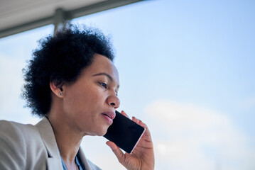 Tensed businesswoman talking on smart phone. Female manager is standing near the window.