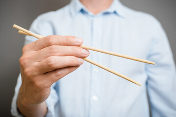 Close-up of unrecognizable caucasian man holding chopsticks of traditional asian food while standing indoors