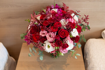 Beautiful bouquet of fresh natural flowers, flowers with very vivid colors in white, marsala, red, pink and green. Bouquet on top of a wooden table and wooden wall behind.