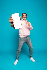 Handsome Excited Man Showing Pointing At Empty Smartphone Screen Posing Over Light Blue Background,...