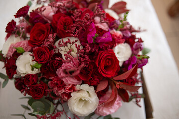 Bouquet of natural and fresh flowers, flowers with vivid colors in marsala, white, red, pink and leaves with green buds. Bouquet on top of a wooden table. Close-up photo with camera zoom.