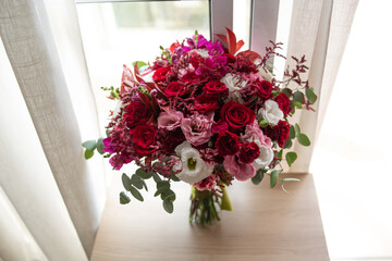 Beautiful bouquet of fresh and natural flowers, colorful flowers in marsala, white, red, pink and leaves with green buds. Diagonal photo with top view. Bouquet on top of a wooden table.