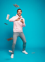 Portrait of a joyful young man holding money cash and celebrating isolated over light blue...