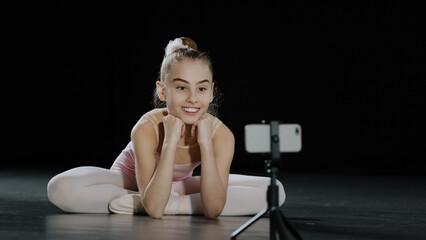 Young teen girl child teenager ballerina gymnast dancer sitting on floor recording vlog waving...