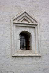 Arched window closed with black iron bars on a old white stucco wall of the monastery. Close-up of Medieval cast-iron shutters on the facade of an old building