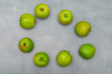 Still life photo of fresh green ripe apples on a grey rustic table. The apples form a circle with copy space in the middle. Still life food photography for many purposes