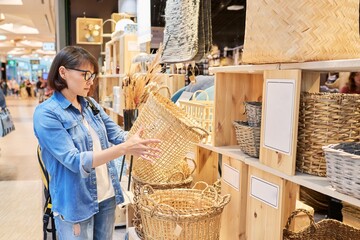 Mature woman shopper choosing interior wicker baskets in home decor store