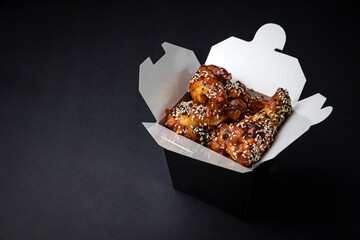 fried chicken wings with sauce and cheese in a delivery box on a black background
