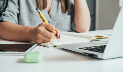 An anonymous businesswoman writing business report while sitting at the kitchen desk with laptop...