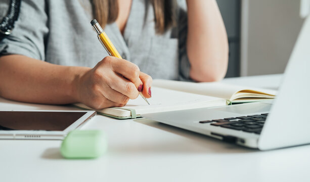 An anonymous businesswoman writing business report while sitting at the kitchen desk with laptop computer, digital tablet and bluetooth earphones